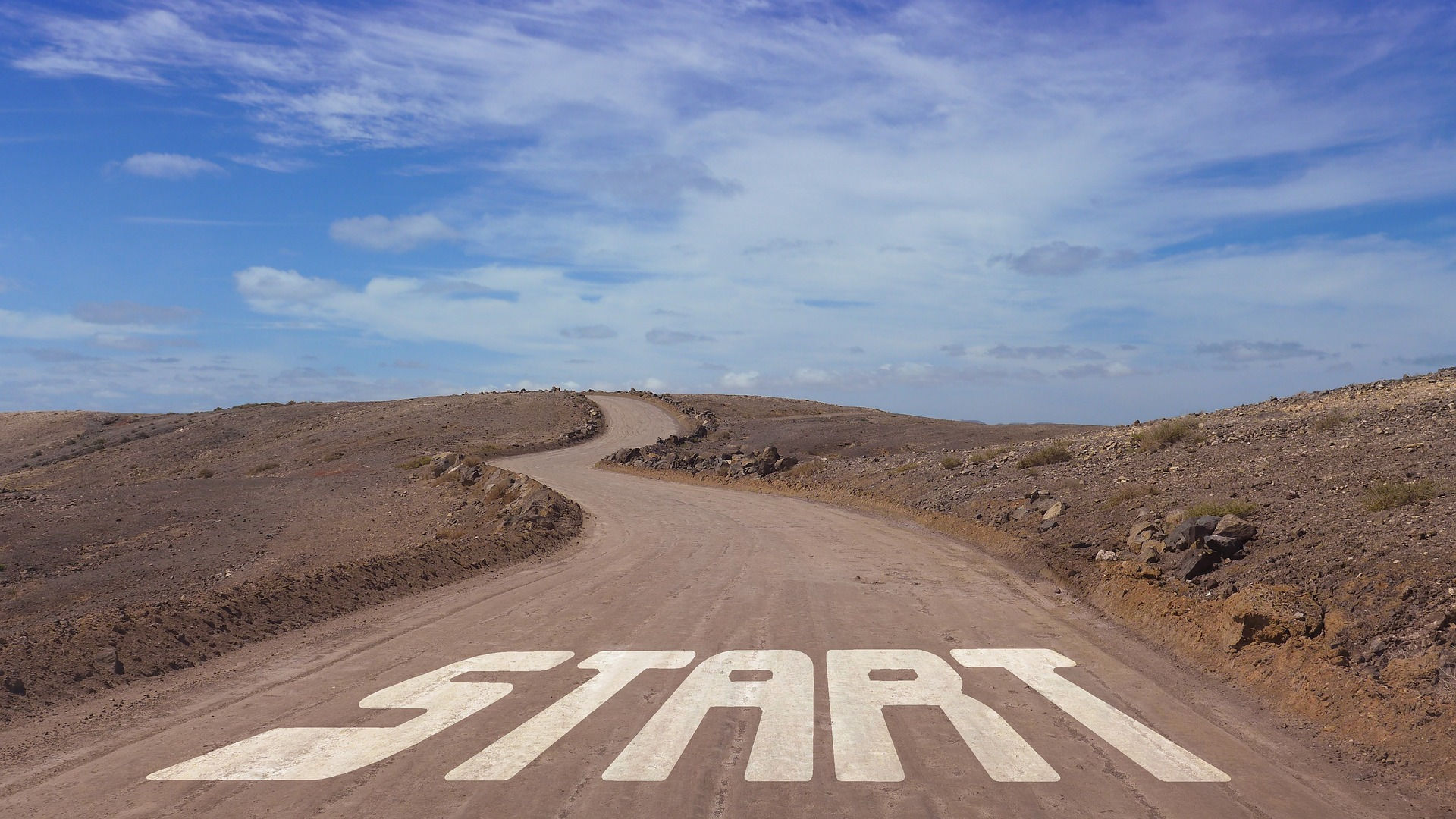 Winding dirt road that goals uphill in a desert area.  At the beginning, "START" is painted on the roadway.